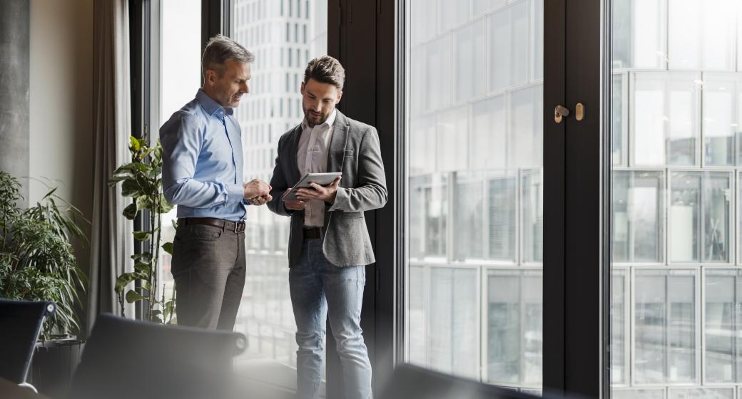 Représentation de deux hommes debout au-dessus regardant une tablette numérique